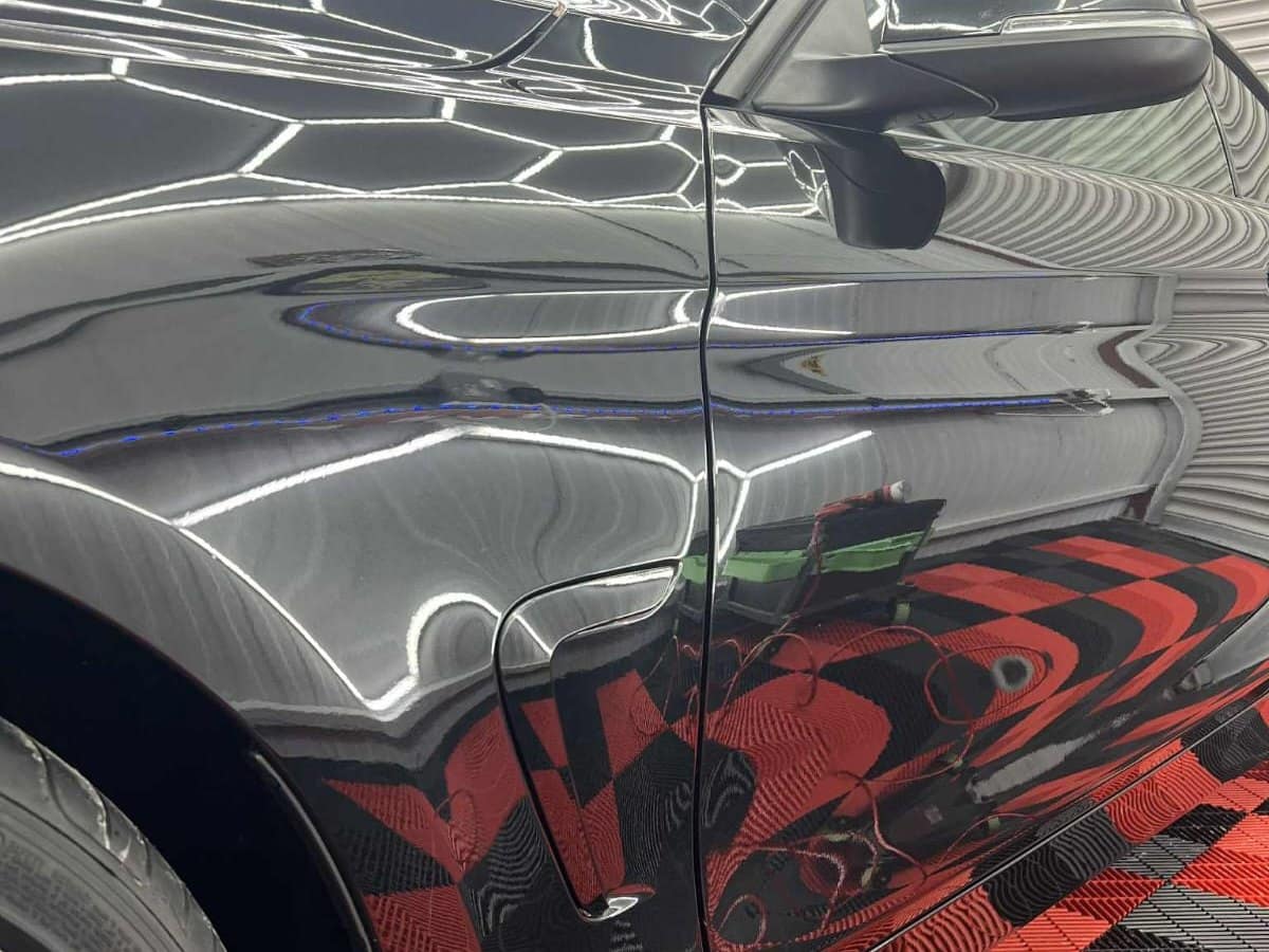 The studio lights reflected in a black BMW's wing after polishing