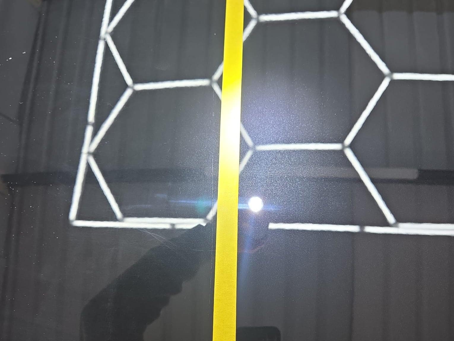 A black Mercedes panel with a tape line under the studio lights, used to compare corrected and uncorrected paint