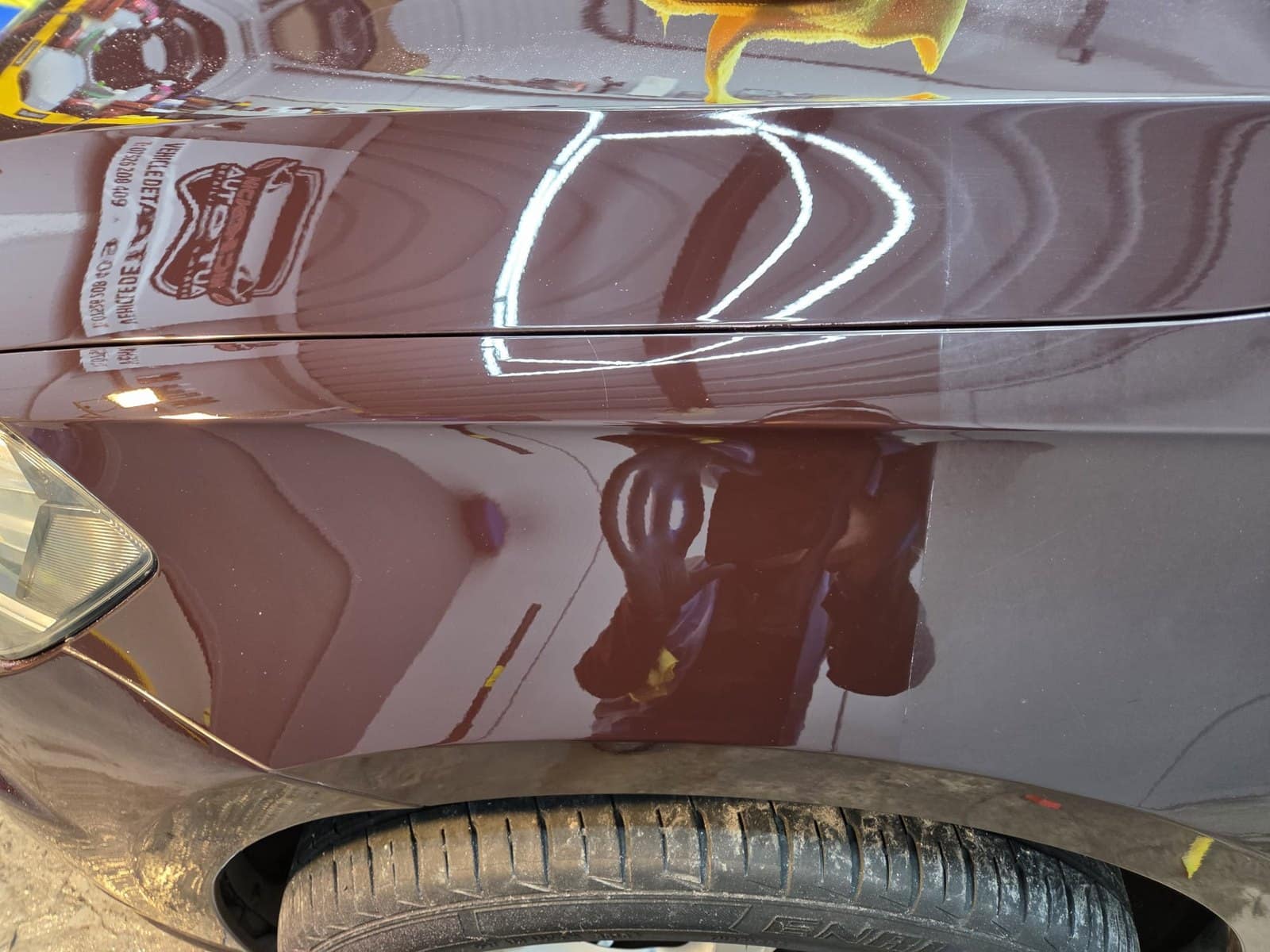 A maroon Volkswagen Golf's wing polished to a mirror finish, the studio reflected in it