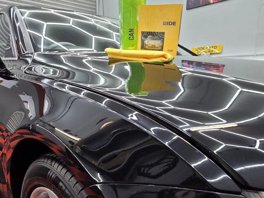 A gloss black car in the studio with a wash mitt and products on the bonnet