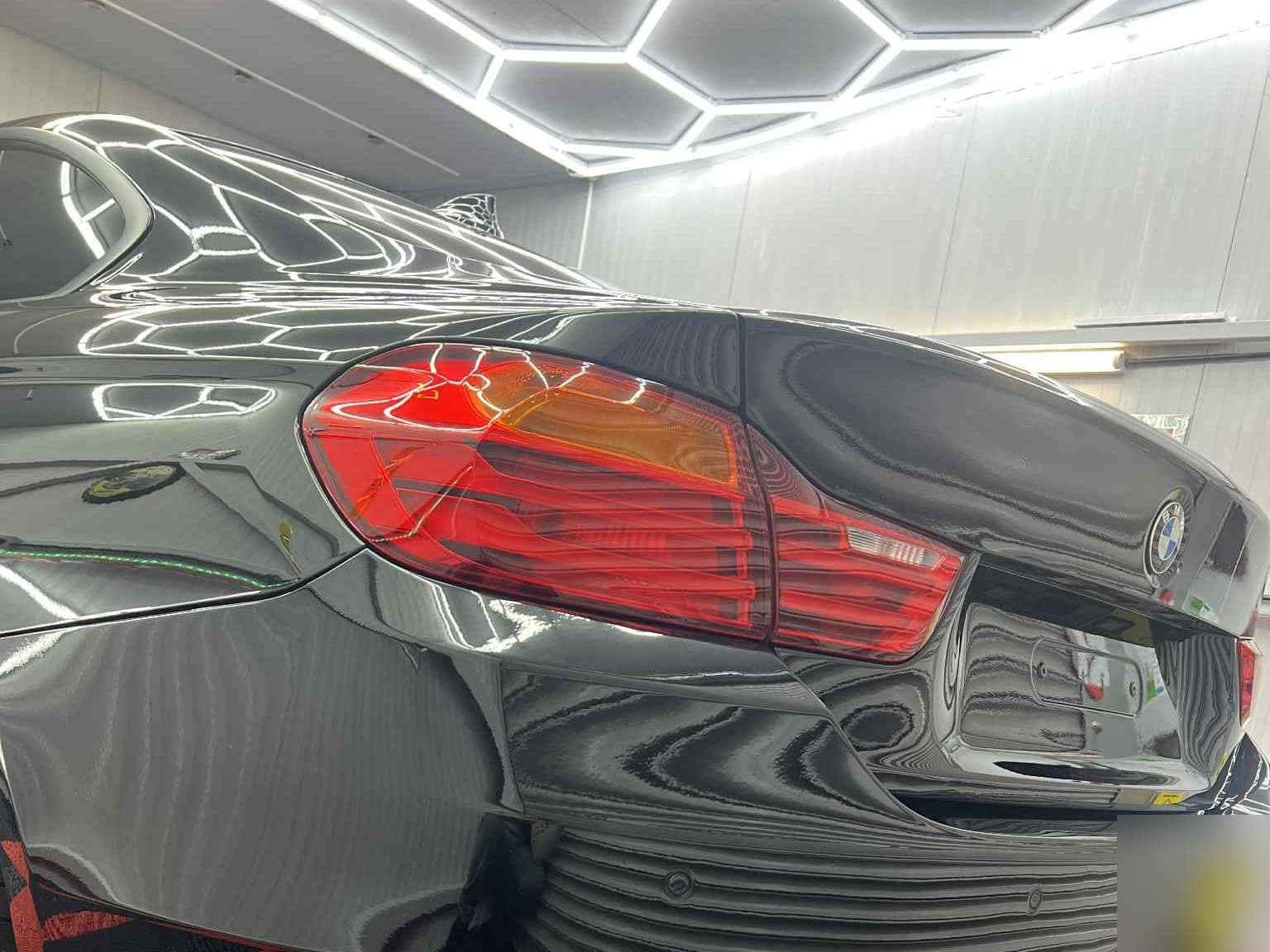 A black BMW after a detail, the studio's hexagon lights reflected in the rear panel