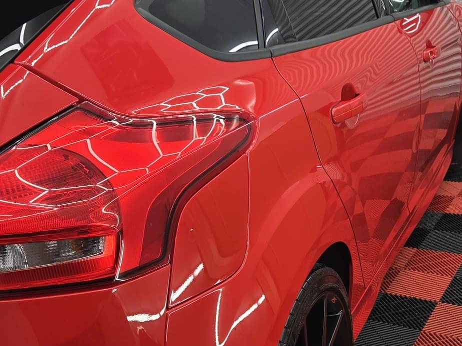 The rear quarter of a red Ford Focus RS with paint protection film, glossy under the studio lights